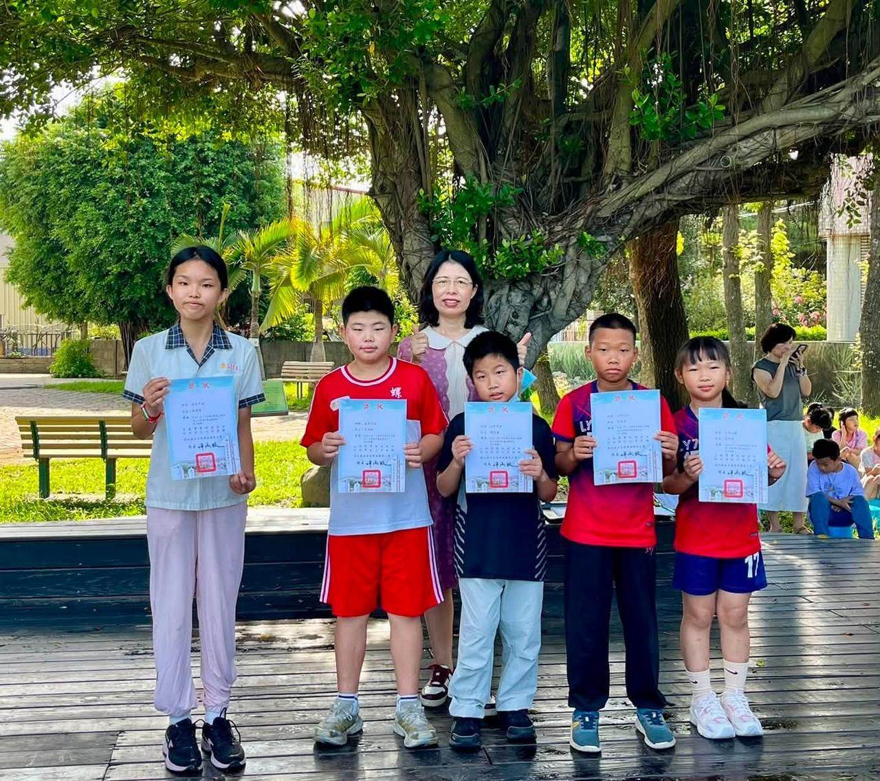 學生與老師在榕樹下領獎合影