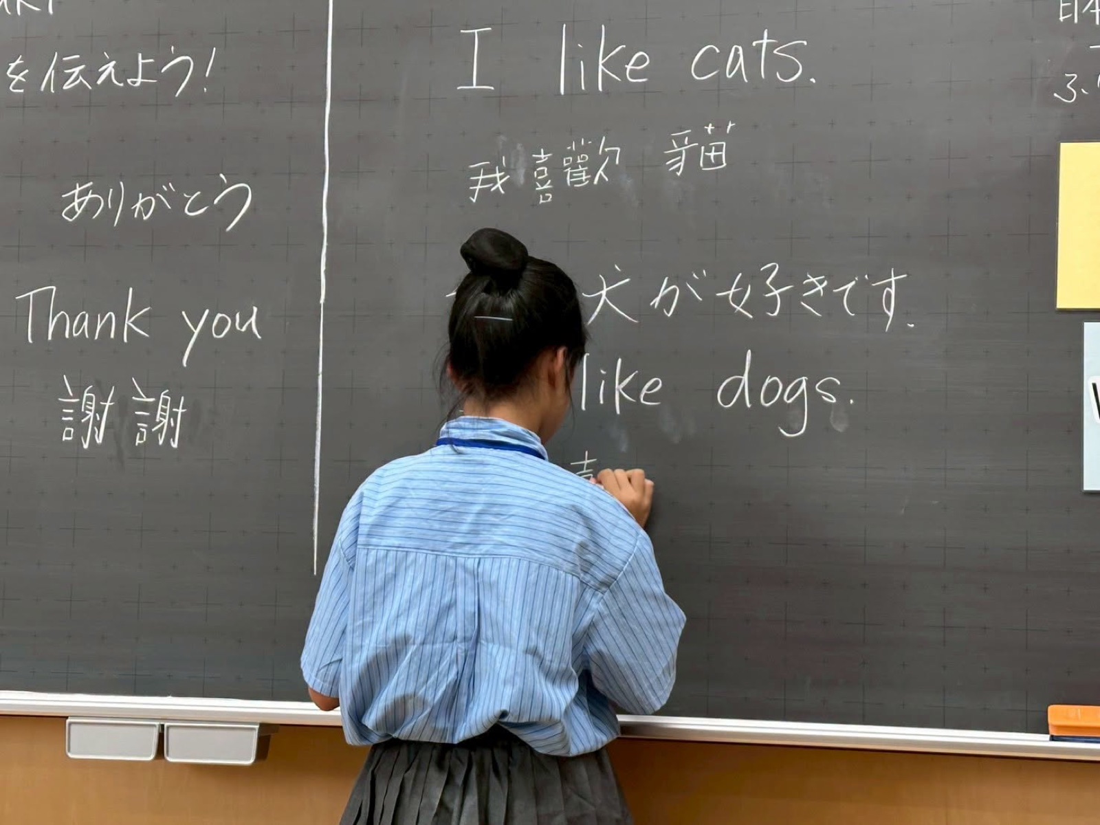 A Japanese student writes bilingual phrases on the blackboard