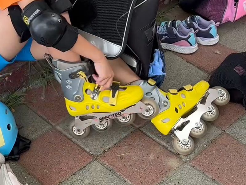A student closing the buckle on a yellow skate · 扣環