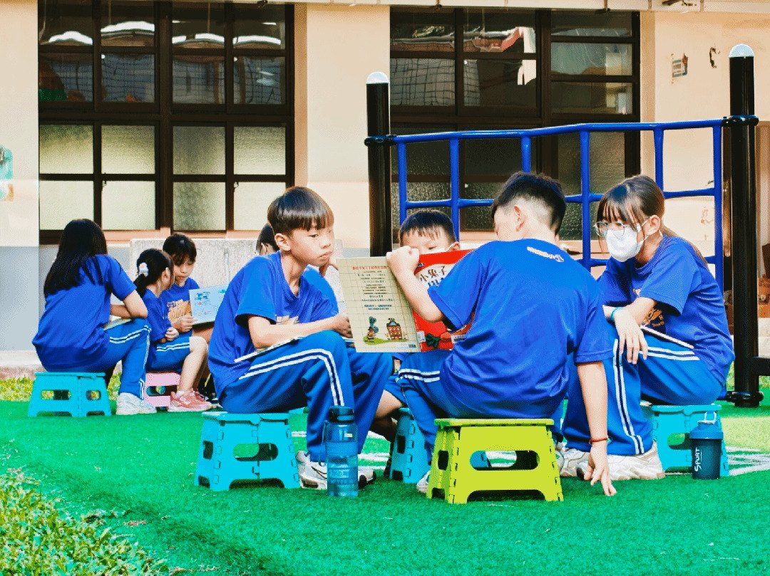 明禮國小學生在校園草地上分組閱讀 Mingli students reading together on the campus lawn