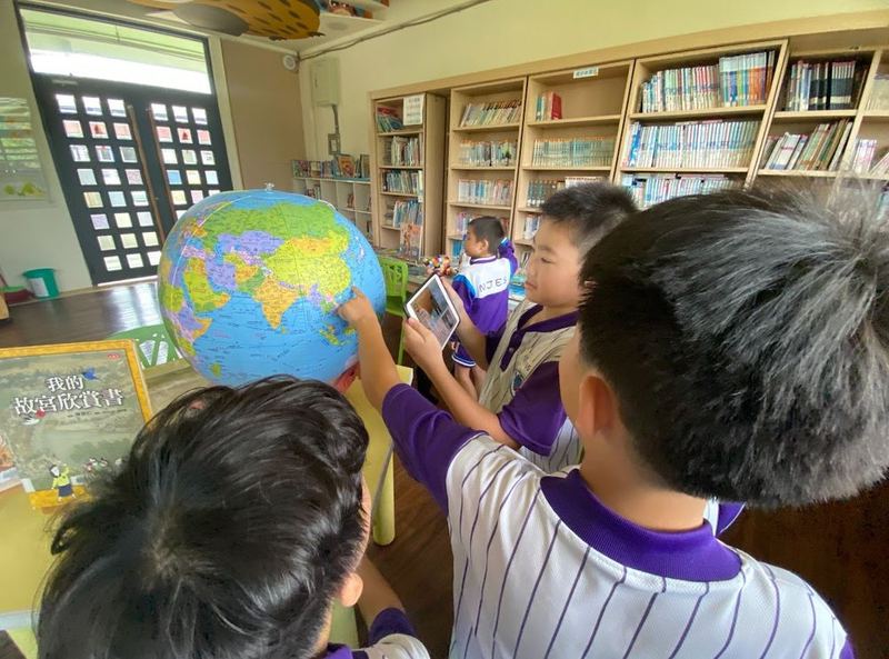 南鎮國小學生在圖書館裡圍著大地球儀，用平板查資料 Nanjen students gathered around a big globe in the library, looking things up on a tablet