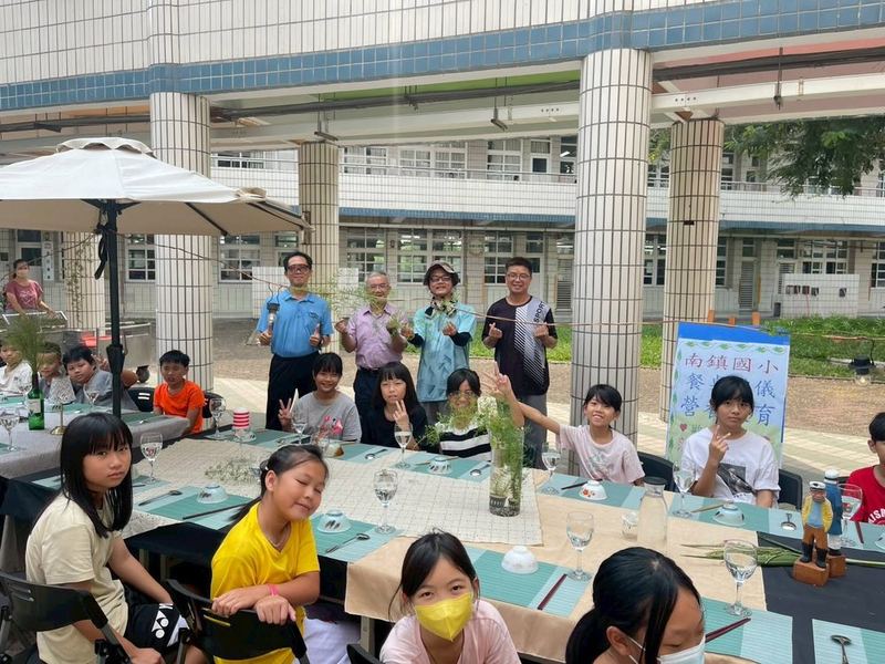 南鎮國小「餐桌禮儀營養教育」活動，學生坐在布置好餐具的長桌旁 Nanjen students at long tables set with tableware during a table-manners and nutrition education event