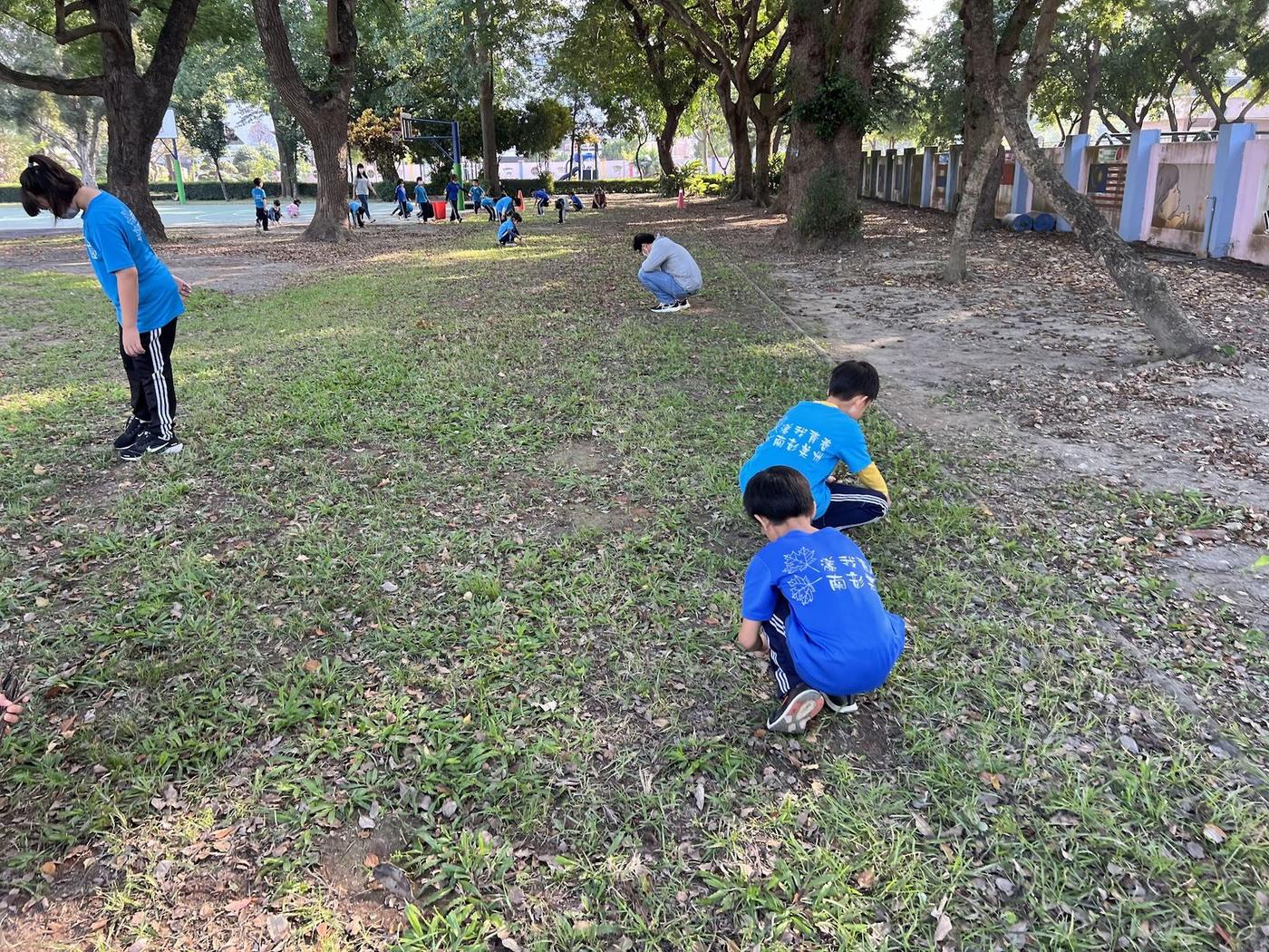 學生蹲在草地上協助清理枯枝雜草