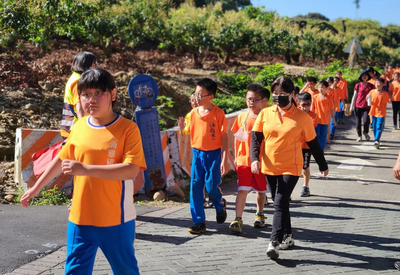 湳雅國小師生穿橘色隊服，沿著果園旁的道路健行踏查