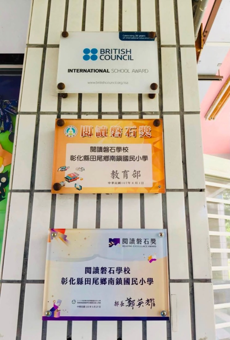 南鎮國小牆上的三面獎牌：英國文化協會國際學校獎與兩面閱讀磐石獎 · Nanzhen's three award plaques: the British Council International School Award and two Reading Excellence Awards