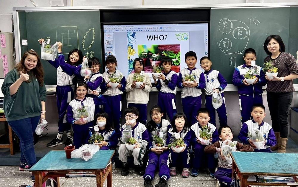 南鎮國小學生在教室裡捧著自己種的植物，和老師一起合照 Nanzhen students in their classroom holding the plants they grew, in a photo with their teachers