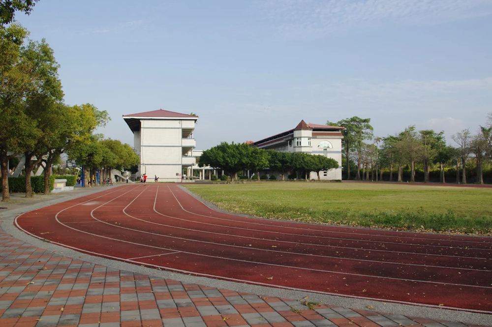 南鎮國小的紅色跑道轉彎處，遠方是校舍與綠樹 The curve of Nanzhen's red running track, with school buildings and trees in the distance