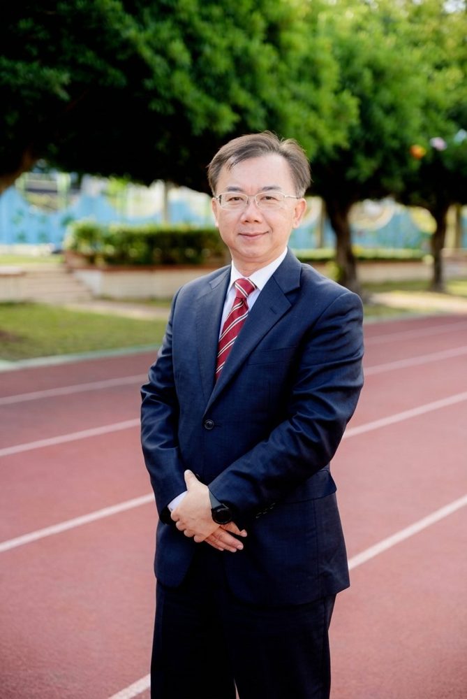 王錦鴻校長身穿深藍色西裝，站在南鎮國小的紅色跑道上 · Principal Wang Chin-hung of Nanzhen Elementary School, in a navy suit on the school's red running track