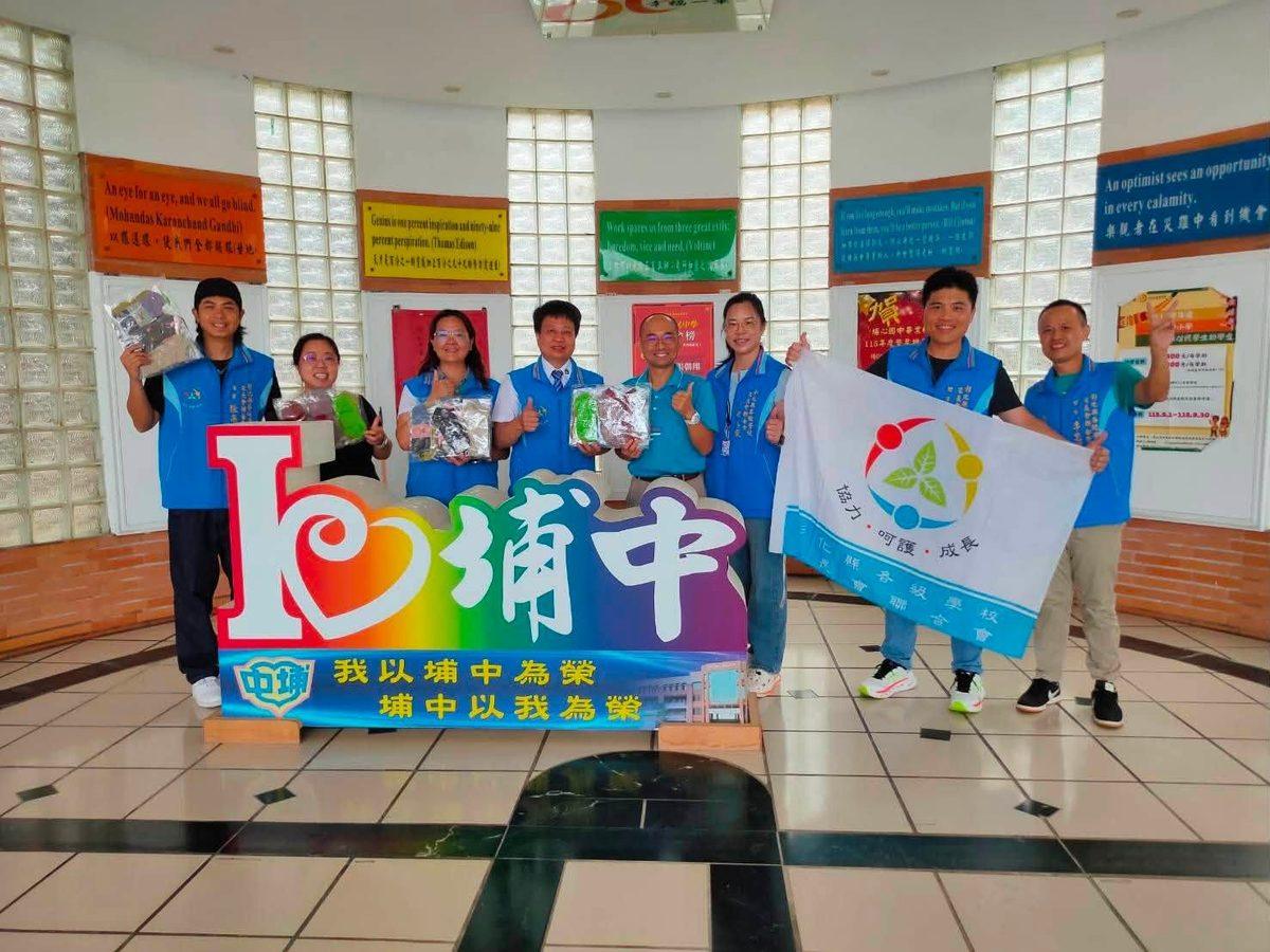家長會聯合會的理監事團隊在埔心國中川堂合影，手持愛心襪、「我愛埔中」彩虹立牌與聯合會會旗 The federation's board members in the Pusin entrance hall with socks, a rainbow 'I ♥ Pusin' sign and the federation flag