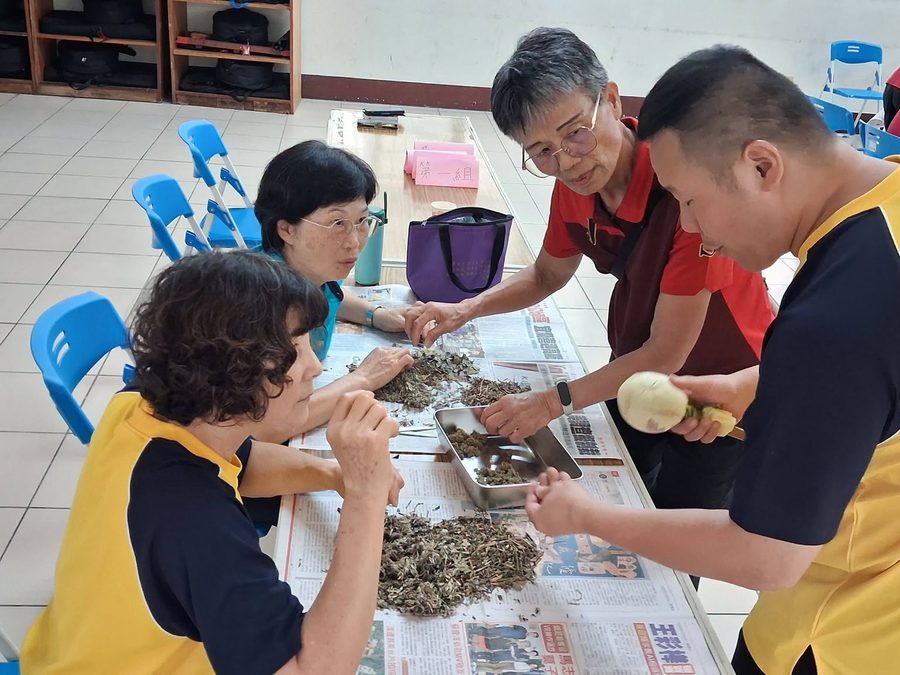 一組學生和志工圍著桌子整理成堆的乾燥香草，桌上放著「第一組」的牌子 A group of students and volunteers around a table sorting piles of dried herbs, a 'Group 1' sign on the table