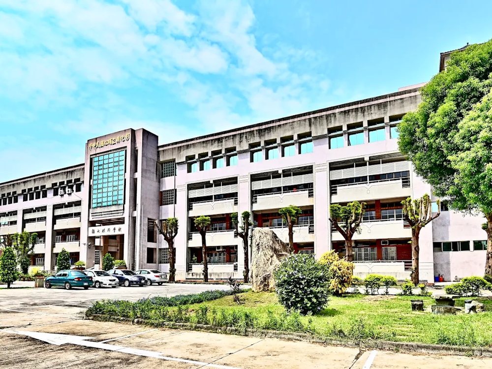 埔心國中行政大樓的長向立面，前方有樹木與草坪，藍天白雲 The long façade of the Pusin administration building, trees and lawn in front, a blue-and-white sky