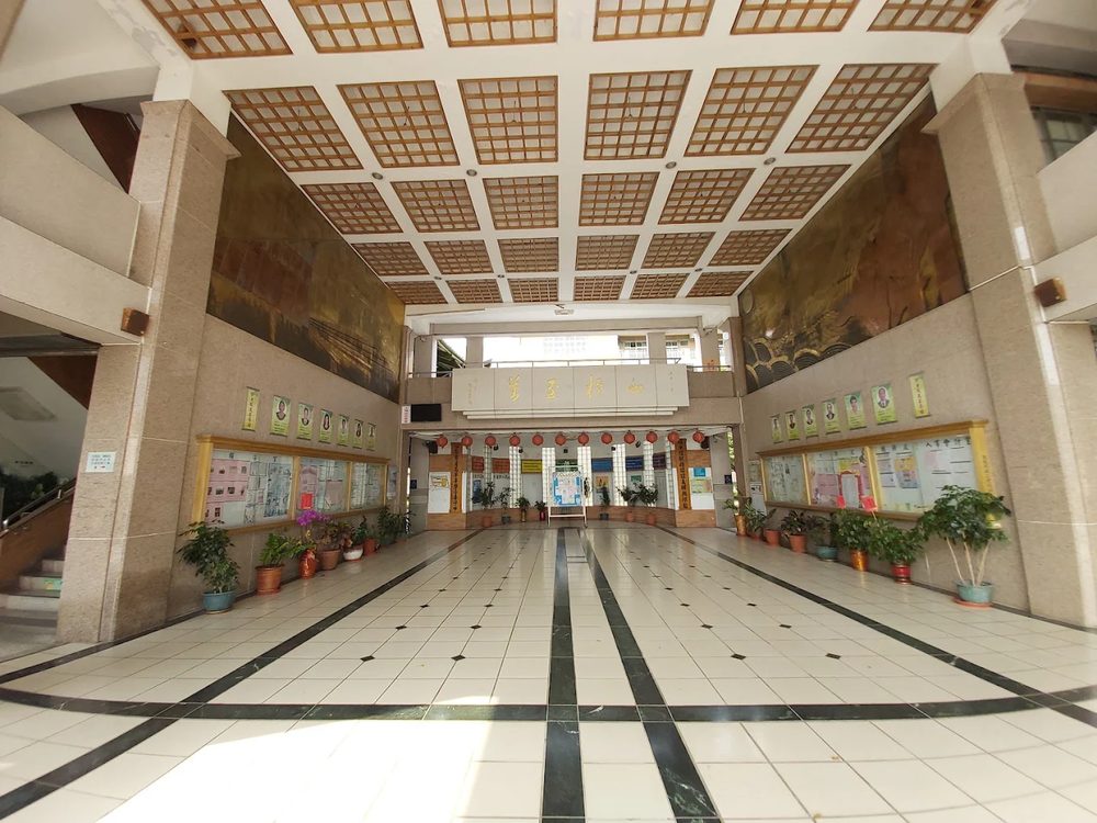 埔心國中挑高的川堂，兩側公布欄與盆栽，中央高處題字「山在毓其英」 The high entrance hall at Pusin, noticeboards and potted plants along both sides, calligraphy set high on the far wall