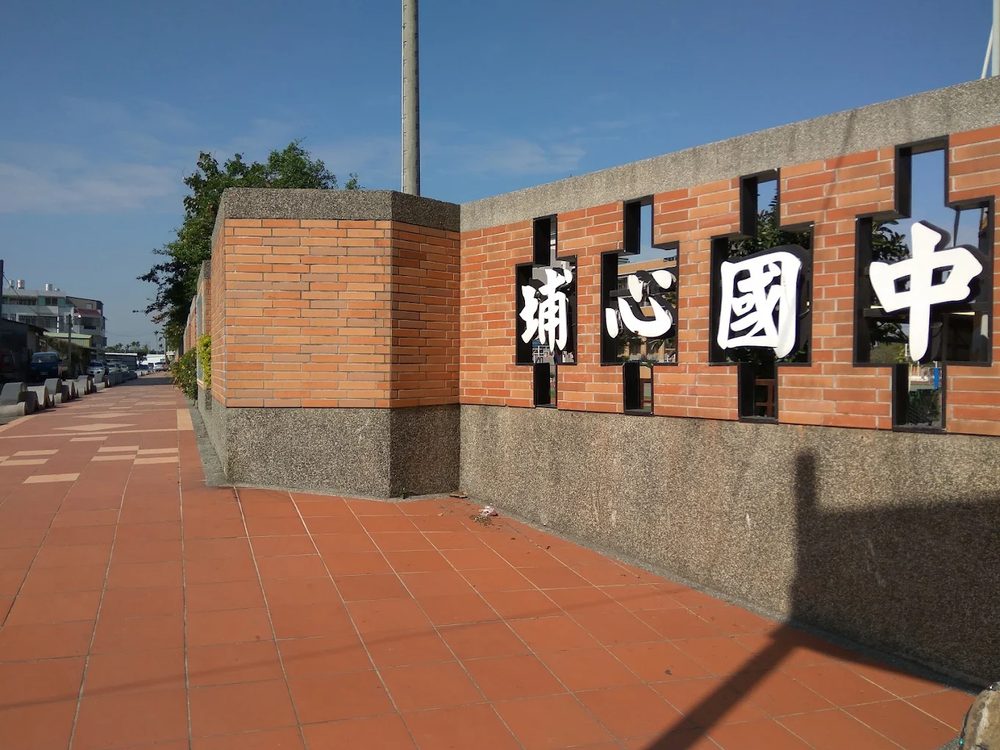 埔心國中紅磚圍牆上鏤空的白色大字「埔心國中」，藍天襯底 The white cut-out characters for 'Pusin Junior High' set into the school's red-brick perimeter wall against a blue sky