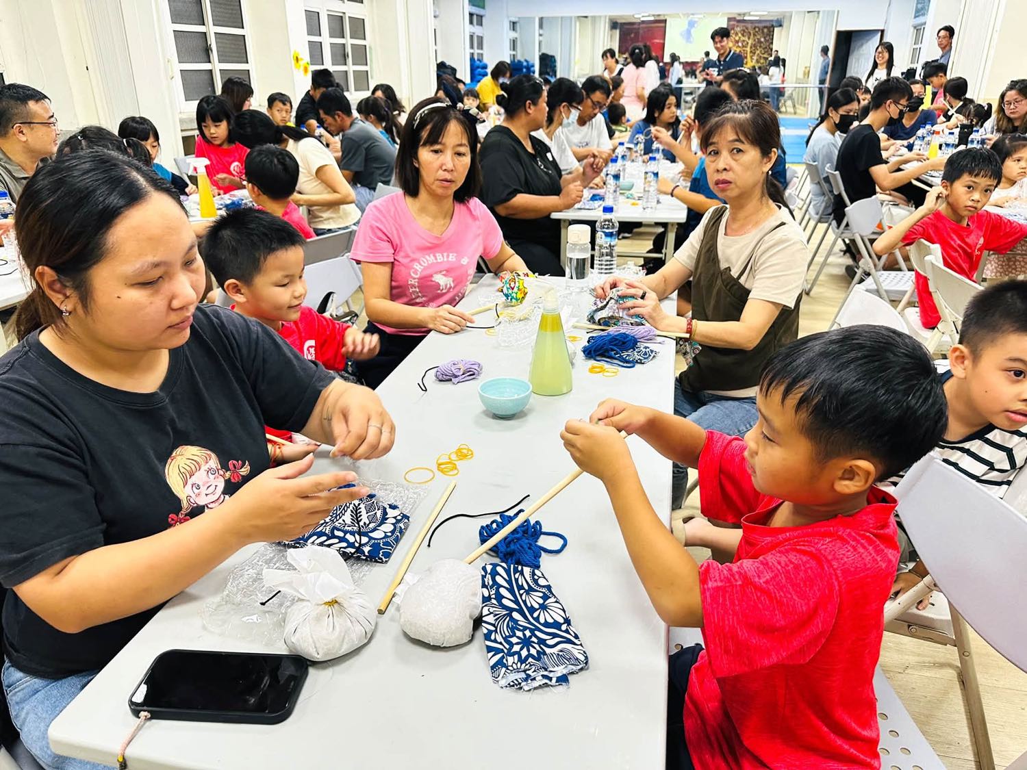 親子在長桌旁一起纏繞棉線，完成自己的艾草棒