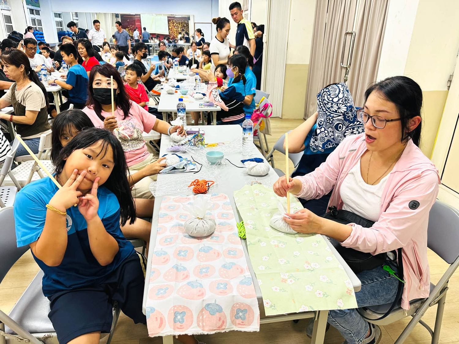 家長與孩子在長桌旁一起把艾草包綁上木棒，做成療癒艾草棒