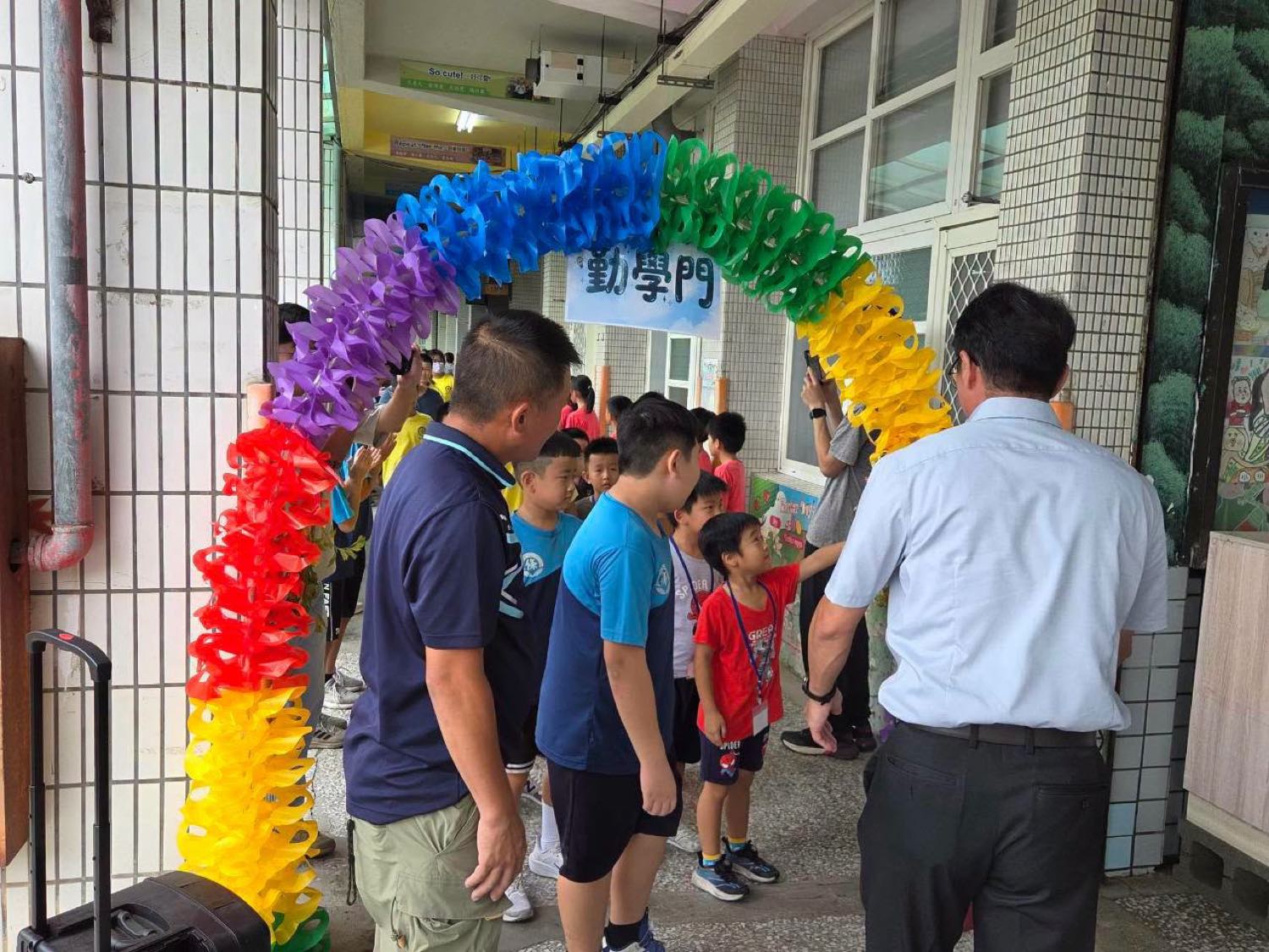 三條國小一年級新生在師長陪伴下跨過彩虹紙花打造的「勤學門」