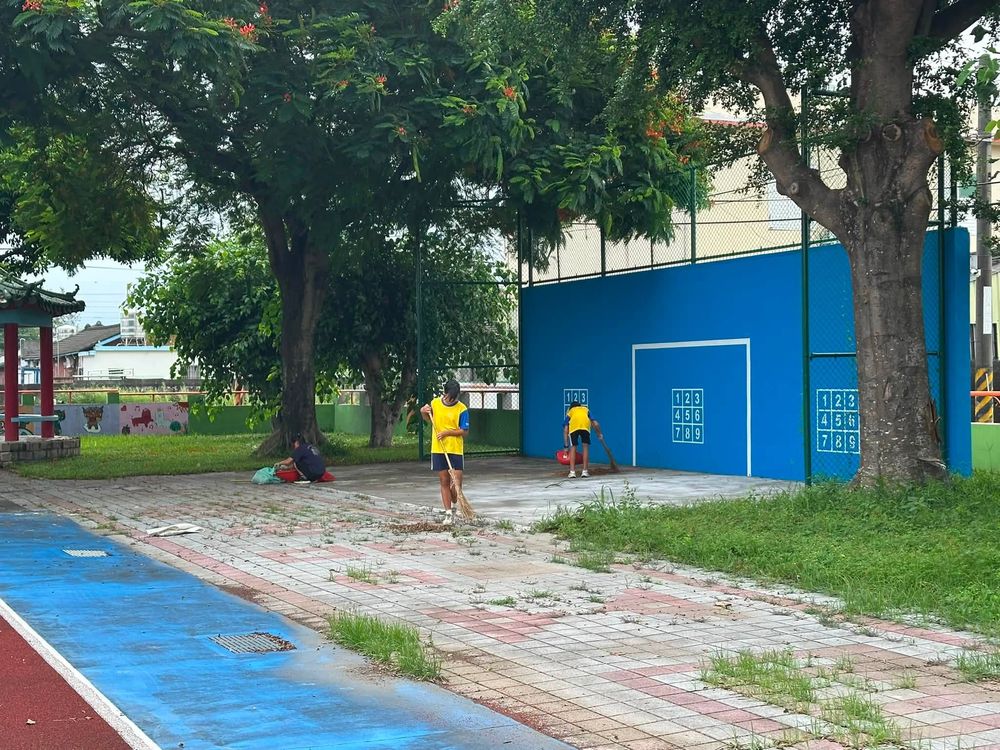 水尾國小學生在藍色牆面前的樹下打掃校園