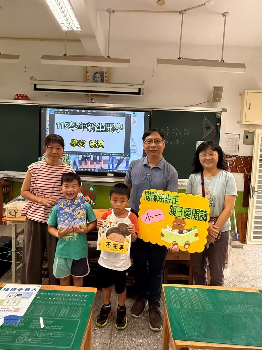 戴豐田校長與兩位小一新生及家長在教室合影，孩子手持繪本
