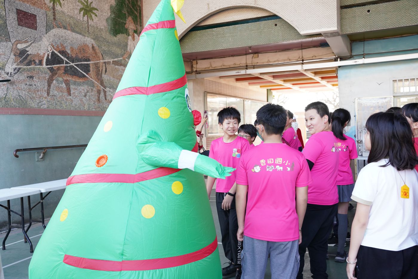Siangtian students in pink school uniforms with a Christmas tree and mosaic wall mural in background