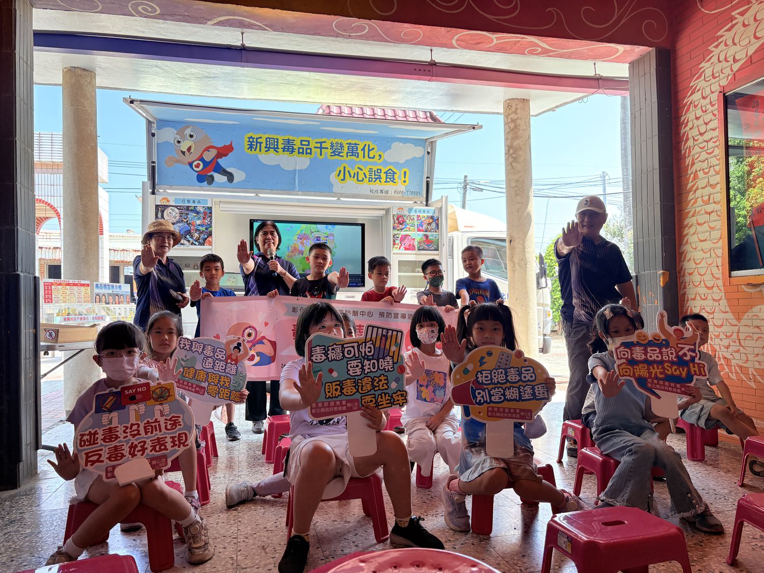 學生在反毒行動車前舉著反毒標語牌合照 Students holding up anti-drug signs in front of the Anti-Drug Mobile Van