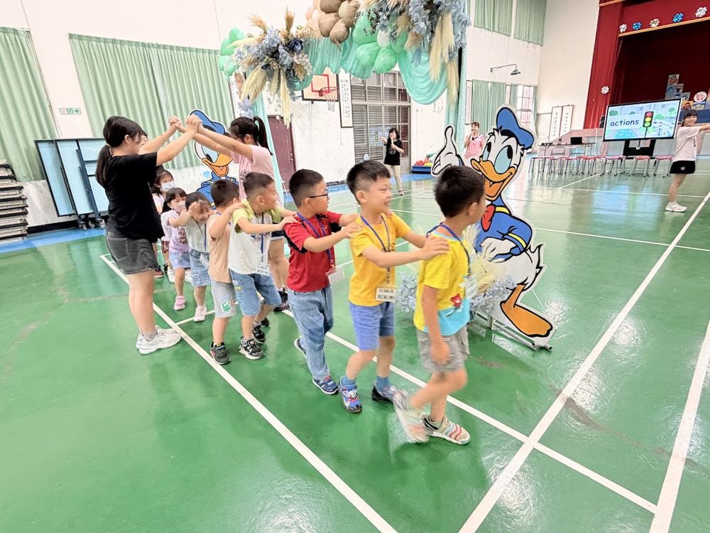 學長姐舉起雙手搭成鐵橋，小一新生排成小火車穿過 Older students raise their arms into a bridge as a line of first graders passes through like a little train
