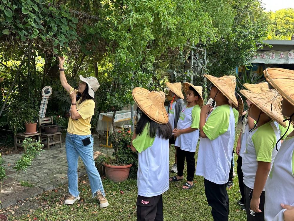 戴著斗笠的學生聽導覽員解說 Students in straw hats listening to a guide outdoors