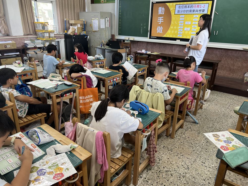 四年甲班學生在教室裡上金融課,黑板螢幕上寫著動手做 Class 4A in a financial-literacy lesson, with a hands-on activity on the screen