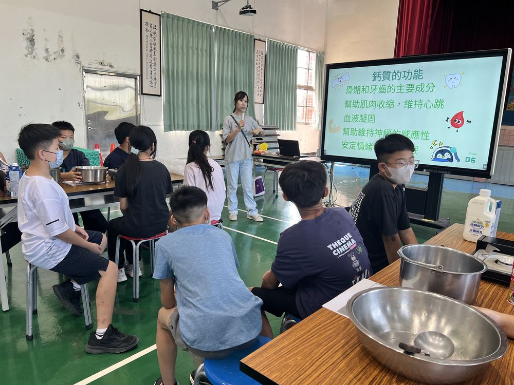 洪老師用投影片講解鈣質的功能 Teacher Hung explaining what calcium does, with a slide on the screen