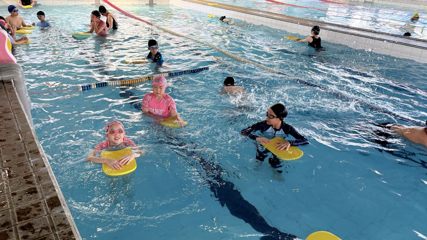 學生在泳池裡扶著浮板練習踢水 Students practicing kicks with kickboards in the pool