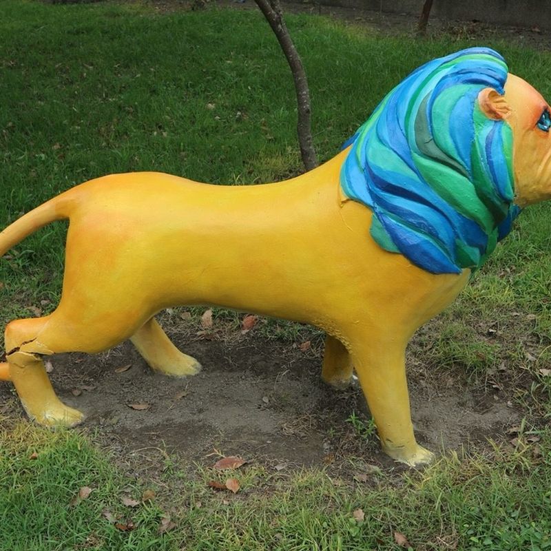 興華國小草地上的黃色彩繪獅子雕塑，有藍綠色的鬃毛 A yellow painted lion sculpture with a blue-green mane on the SingHua lawn