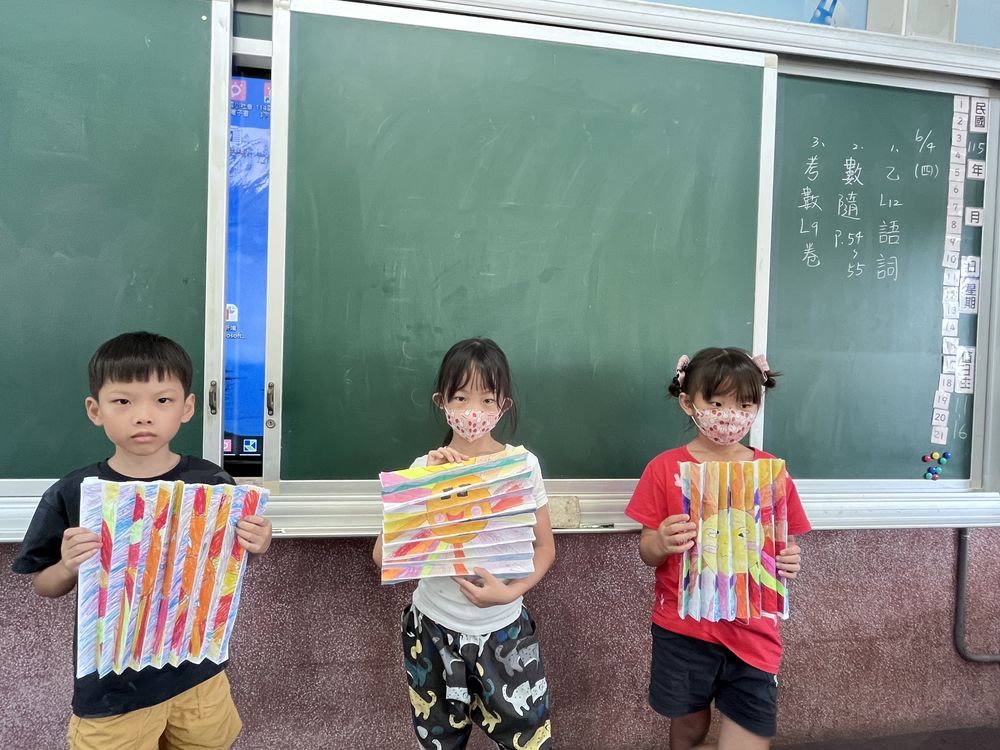 三位學生在黑板前拿著色彩繽紛的作品 Three students holding up their colorful artwork in front of the blackboard