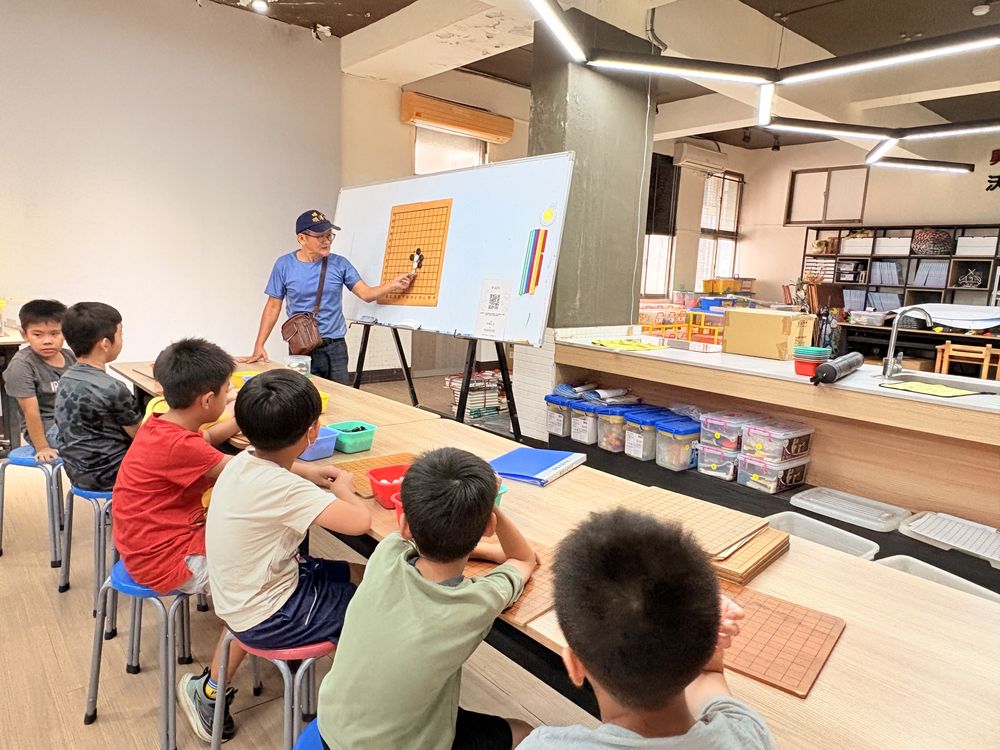圍棋社老師在白板前講解棋局,學生坐著聽 A Go Club teacher explaining a game at the whiteboard while students listen