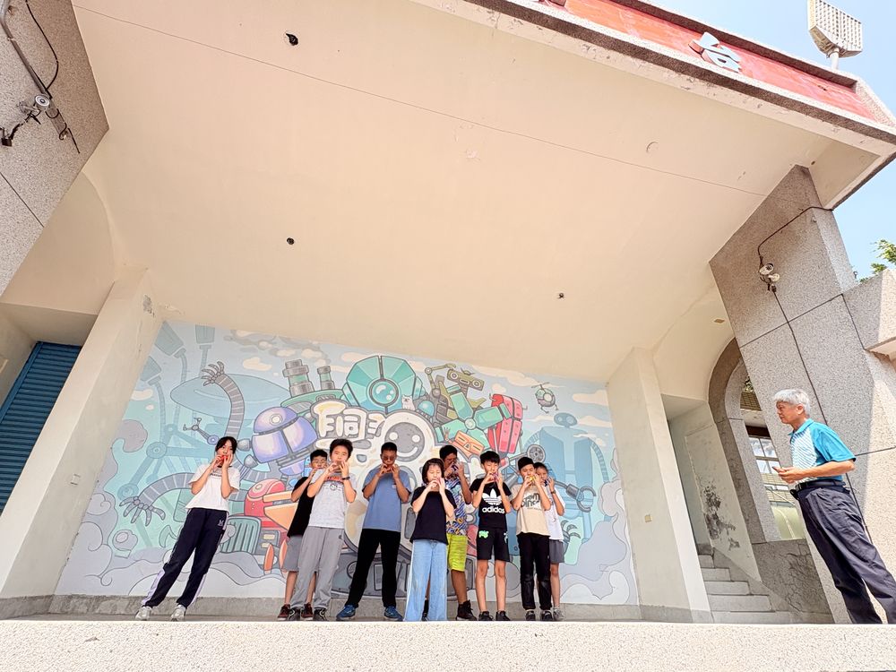 陶笛社學生在彩繪牆前的舞台上演奏 Ocarina Club students playing on a stage in front of a painted wall