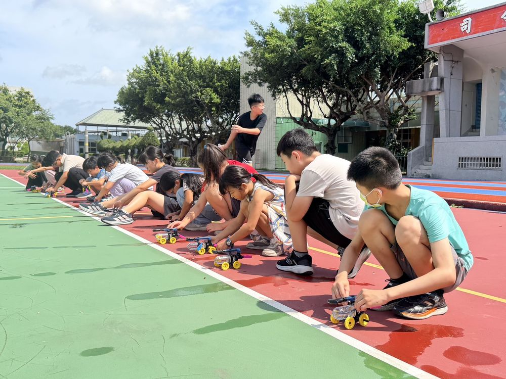 學生蹲在跑道上,把親手組裝的小車排成一列 Students crouching on the track, lining up the little cars they built