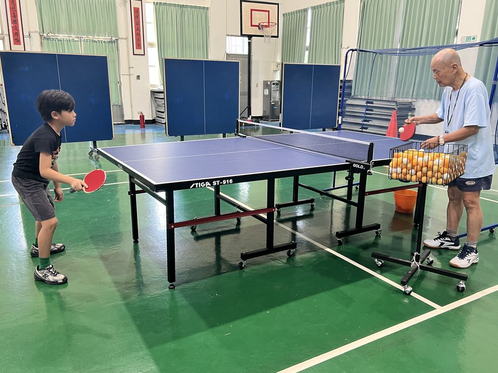 桌球社學生揮拍擊球，教練在對面餵球 A Table Tennis Club member hitting the ball as the coach feeds balls from the other side