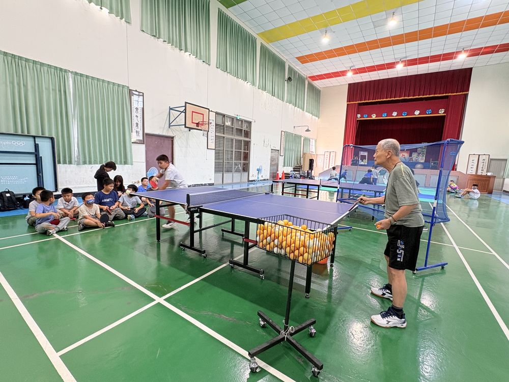 教練在球桌旁指導，其他社員在一旁觀看 The coach working at the table while other club members watch