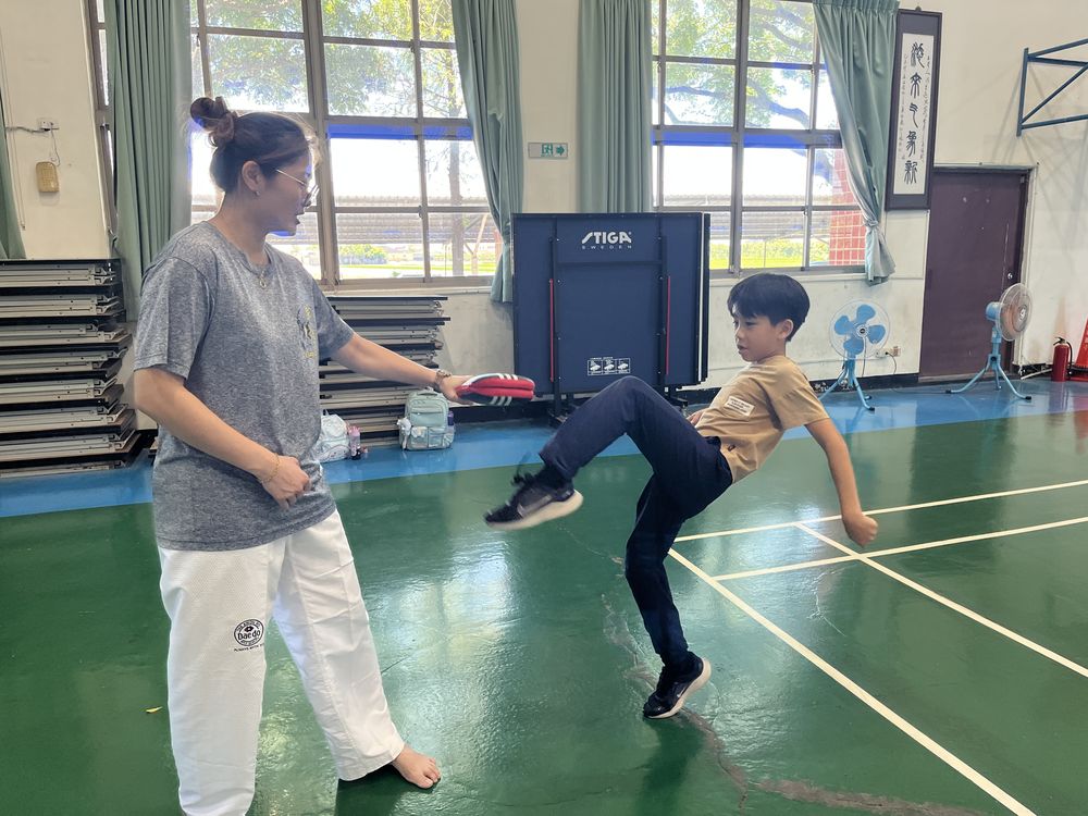 學生高高抬腿踢擊，教練在旁指導 A student doing a high kick while the coach watches and guides
