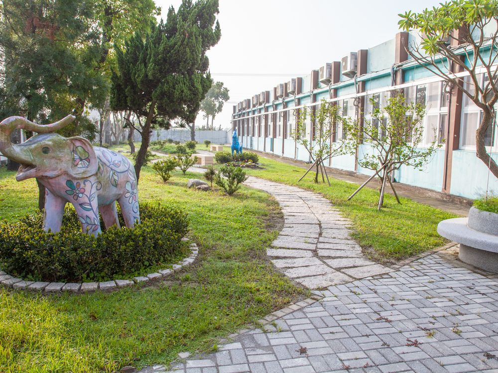 興華國小石板步道旁的彩繪大象雕塑，旁邊是教室 A painted elephant sculpture beside a stone garden path, with classrooms alongside
