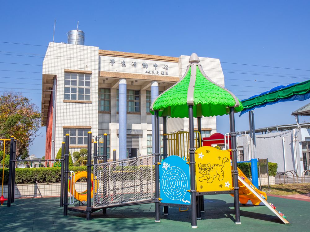 興華國小遊戲場，有綠色屋頂的溜滑梯與迷宮板，後方是學生活動中心 The SingHua playground, with a green-roofed slide set and the Student Activity Center behind