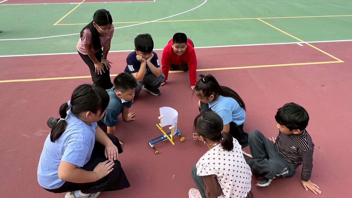 興華國小學生圍坐在球場上，一起看著自己組裝的作品 SingHua students sitting in a circle on the court, watching a model they built together
