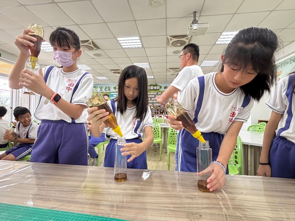 田中國小學生專注地將蜂蜜倒入玻璃瓶中