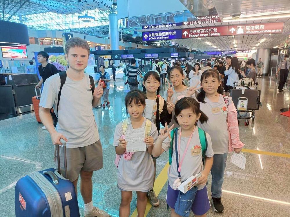田中國小學生在機場出境大廳與外國旅客合影並展示填寫完成的英語任務單