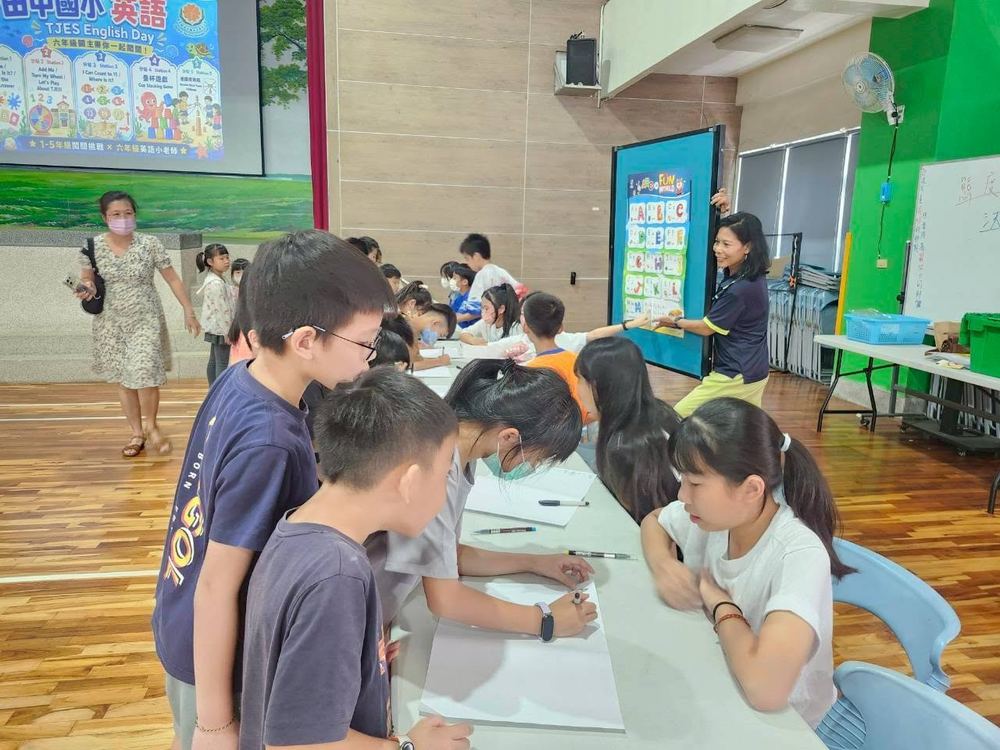 田中國小學生在英語日分站前排隊寫學習單，關主拿著字母字卡