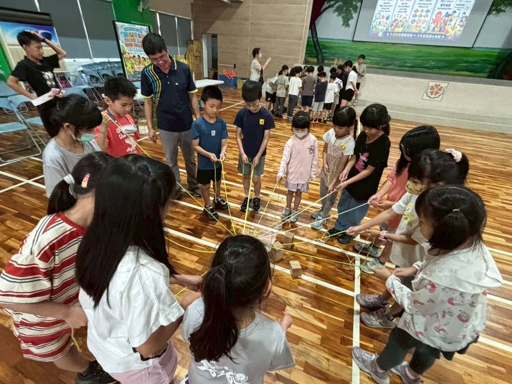 田中國小學生圍成一圈，各拉一條繩子合力堆疊木塊的團隊挑戰