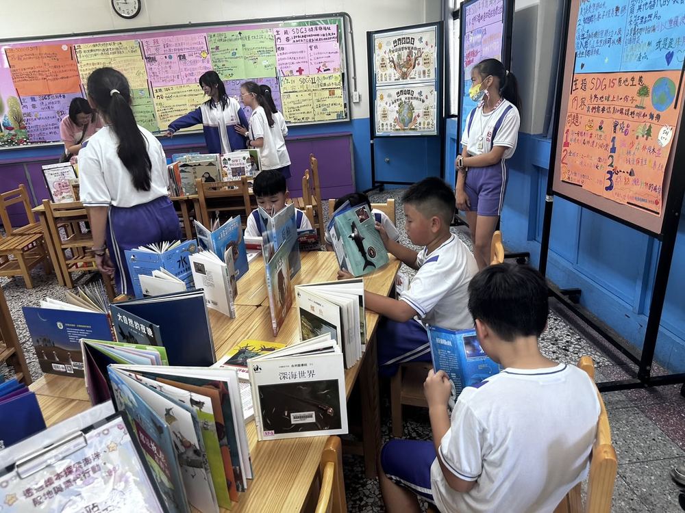 田中國小 SDGs 主題書展現場，學生坐在長桌邊翻閱自然與海洋主題書籍，牆上貼滿手繪海報