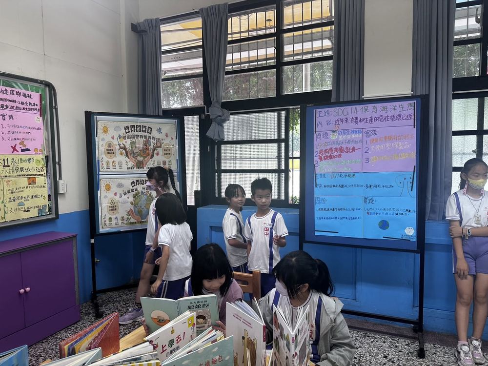 田中國小學生在 SDG14 保育海洋生態海報與世界閱讀日海報前閱讀繪本