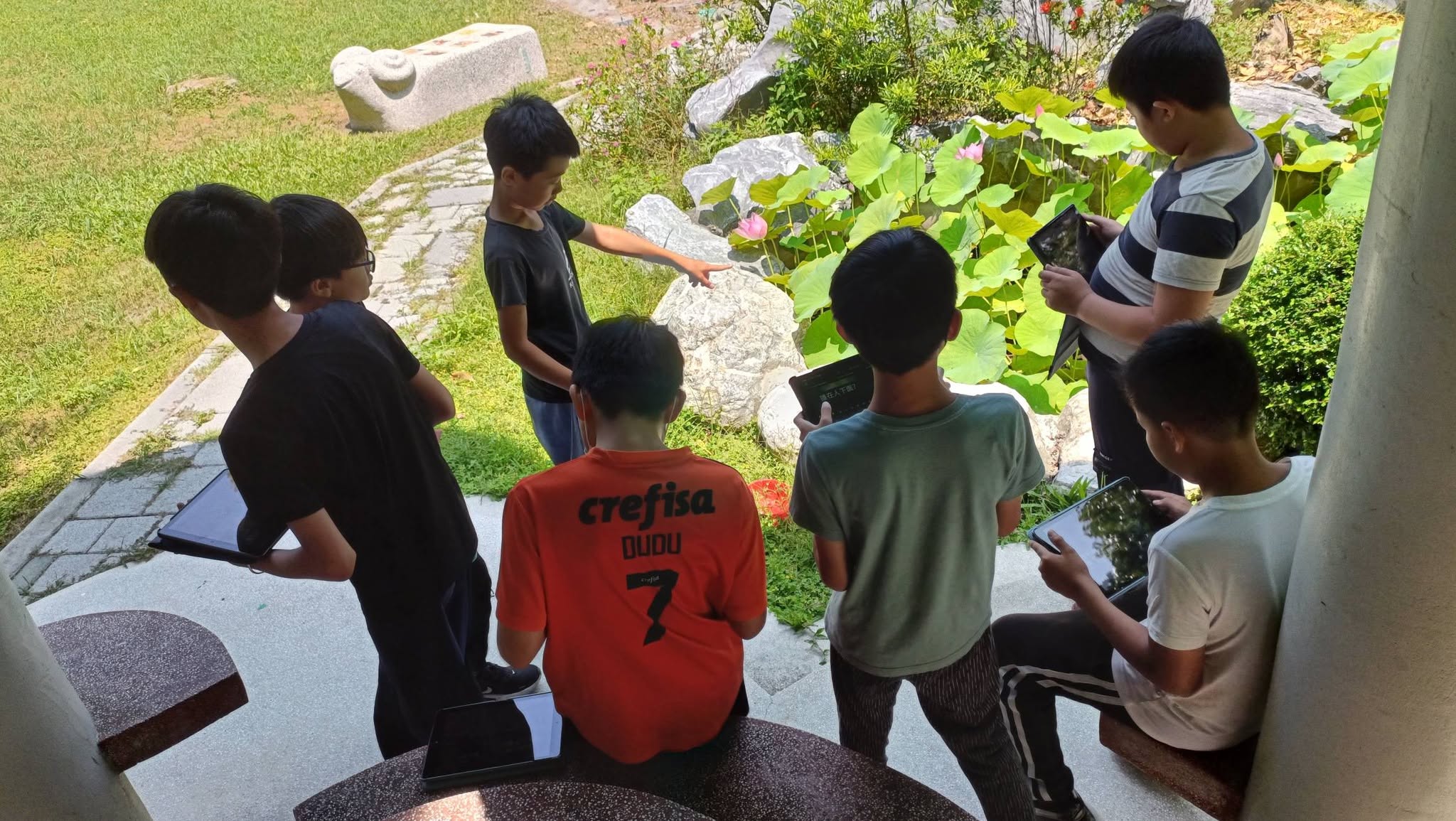 Students pointing at clues near the garden pond, heads together