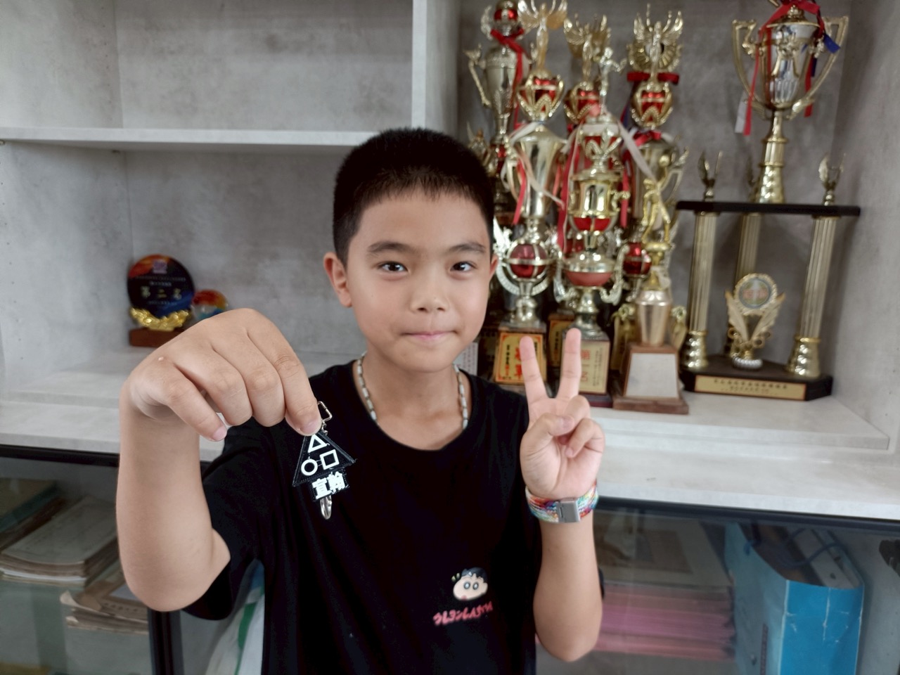 A student showing a 3D-printed keychain in front of the trophy shelf