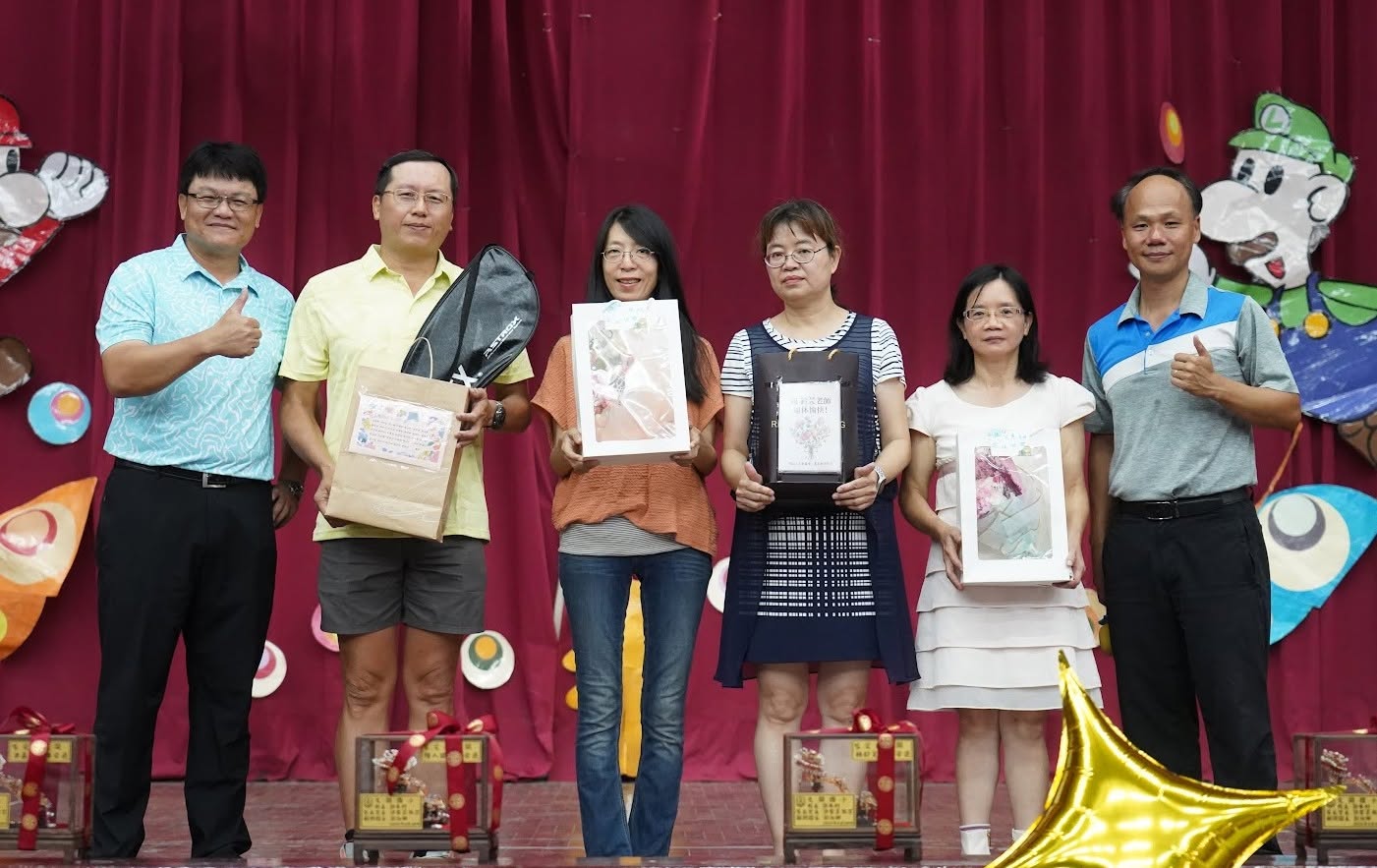 Retiring teachers holding farewell gifts on stage