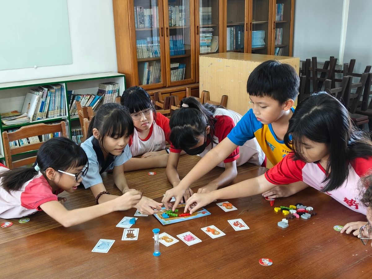 學生們圍著桌子玩桌遊，把動物放上船